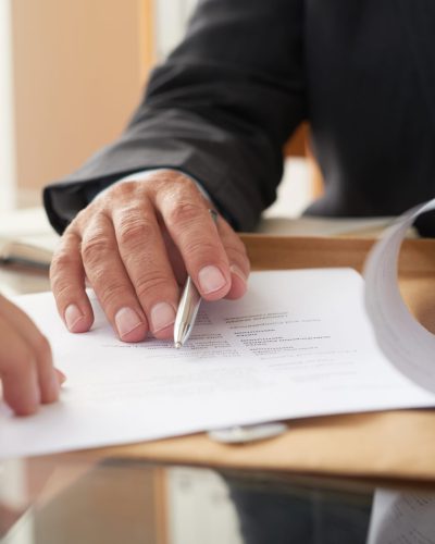 Close-up of businessman examining business contract and signing it at the office desk