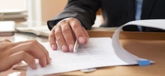 Close-up of businessman examining business contract and signing it at the office desk