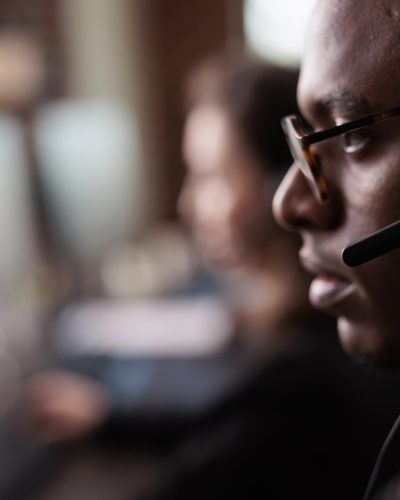 Helpdesk secretary listening to client on helpline call, using customer service network on headset. Male receptionist working at call center telemarketing assistance. Close up.