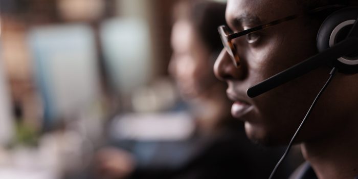 Helpdesk secretary listening to client on helpline call, using customer service network on headset. Male receptionist working at call center telemarketing assistance. Close up.