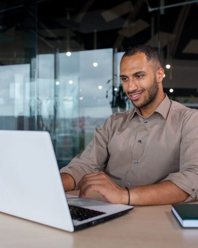 Young successful businessman working inside the office with a laptop, satisfied with the results of the achievement, the man is smiling, typing on the keyboard.